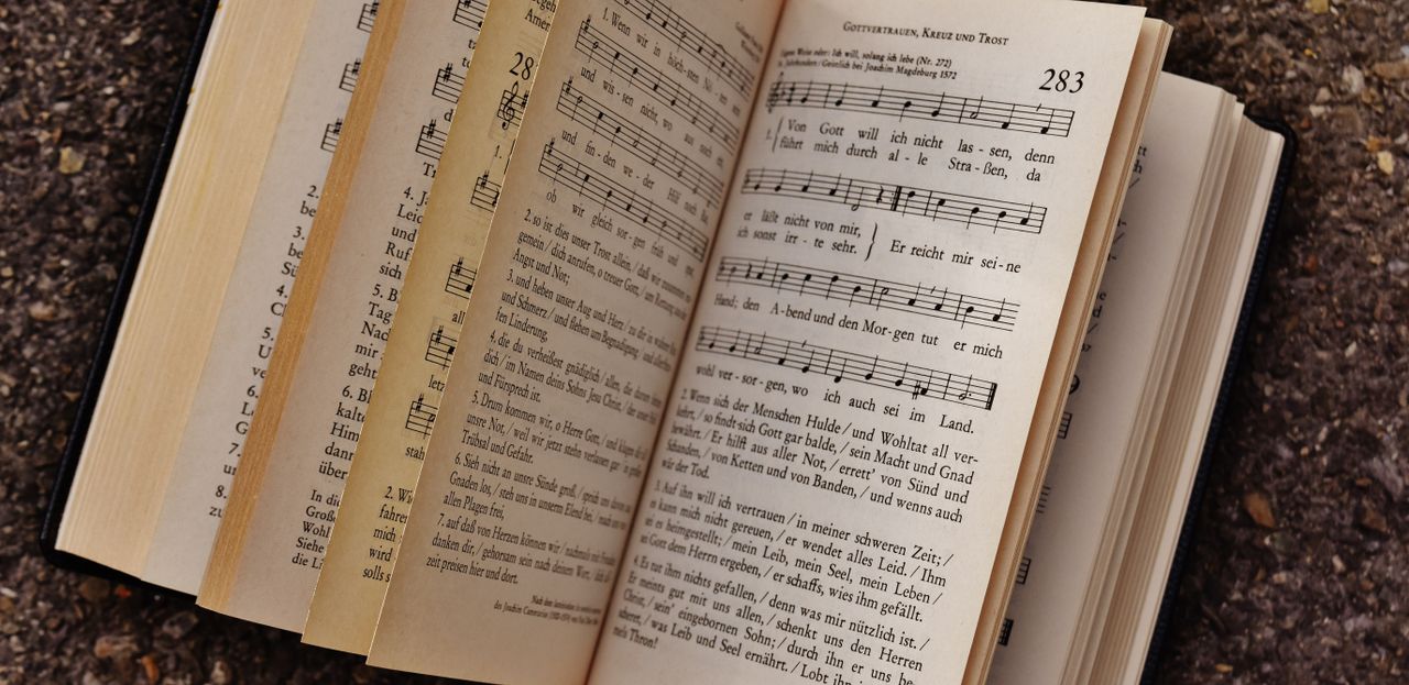 Close-up of an open book displaying musical notes and lyrics on a textured ground surface.